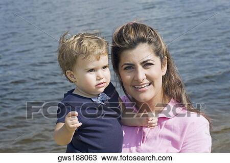 Portrait of a mid adult woman carrying her son and smiling View Large Photo Image Stock Image - Portrait of a mid adult woman carrying her son and smiling. Fotosearch