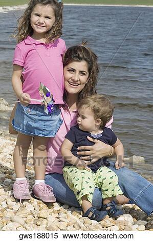 Portrait of a mid adult woman sitting on stones with her two children at the water's edge View Large Photo Image Stock Photography - Portrait of a mid adult woman sitting on stones with her two children at the water's edge. Fotosearch