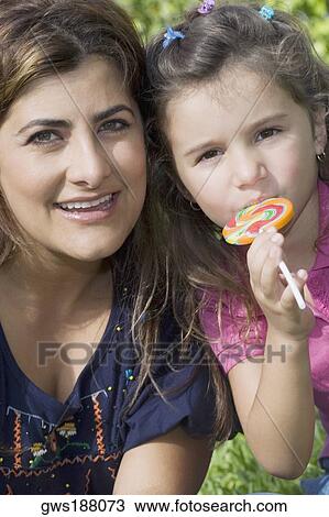 Portrait of a mid adult woman smiling with her daughter eating a candy View Large Photo Image Stock Image - Portrait of a mid adult woman smiling with her daughter eating a candy. Fotosearch