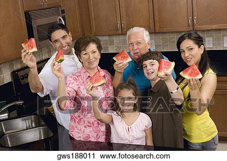Stock Image - Portrait of a three generation family holding slices of a watermelon in the kitchen. Fotosearch