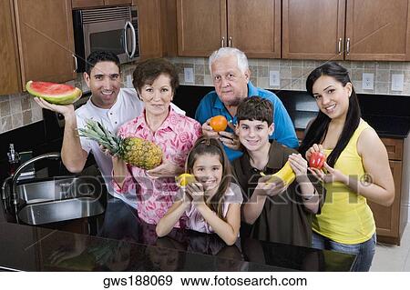 Stock Photo - Portrait of a three generation family holding fruits in the kitchen. Fotosearch