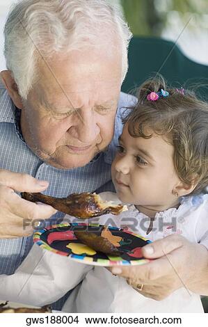Senior man feeding chicken to his granddaughter View Large Photo Image Picture - Senior man feeding chicken to his granddaughter. Fotosearch