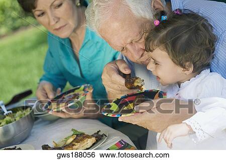Senior man feeding chicken to his granddaughter with a senior woman sitting beside them View Large Photo Image Stock Photograph - Senior man feeding chicken to his granddaughter with a senior woman sitting beside them. Fotosearch