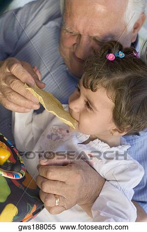 Stock Photography - Senior man feeding papadam to her granddaughter. Fotosearch