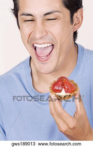 Stock Image - Close-up of a young man holding a strawberry tart and laughing. Fotosearch