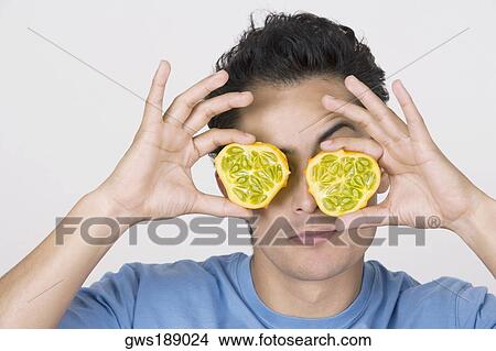 Close-up of a young man holding two halves of a kawani fruit in front of his eyes View Large Photo Image Picture - Close-up of a young man holding two halves of a kawani fruit in front of his eyes. Fotosearch