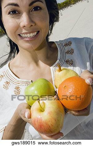 Stock Photography - Portrait of a mid adult woman holding fruits and smiling. Fotosearch