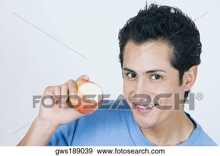 Stock Photo - Portrait of a young man showing a missing bite apple and smiling. Fotosearch
