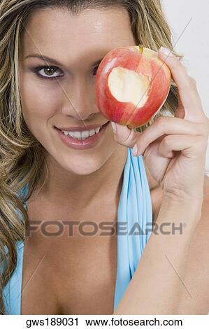 Stock Image - Portrait of a young woman holding a missing bite apple and smiling. Fotosearch
