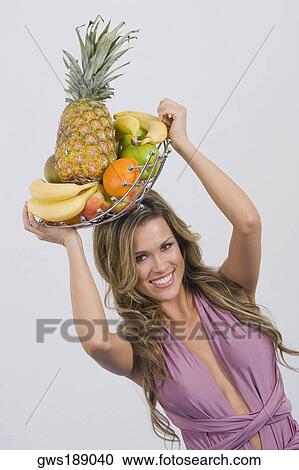 Stock Image - Portrait of a young woman holding a basket of assorted fruits and smiling. Fotosearch
