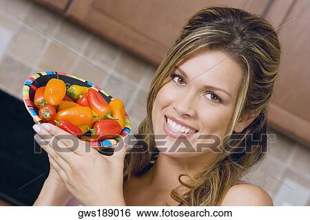 Stock Photograph - Portrait of a young woman holding a plate of red chili peppers. Fotosearch
