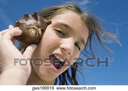 Portrait of a girl holding a conch shell to her ear View Large Photo Image Stock Photo - Portrait of a girl holding a conch shell to her ear. Fotosearch