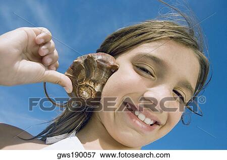 Portrait of a girl holding a conch shell to her ear and smiling View Large Photo Image Stock Photo - Portrait of a girl holding a conch shell to her ear and smiling. Fotosearch
