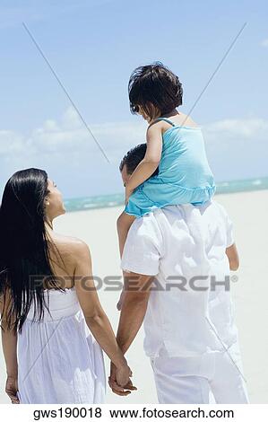 Stock Photo - Rear view of a mid adult man carrying his daughter on his shoulders with a mid adult woman beside them. Fotosearch