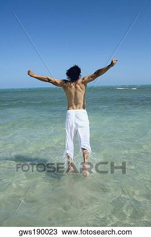 Rear view of a mid adult man jumping on the beach with his arms outstretched View Large Photo Image Stock Image - Rear view of a mid adult man jumping on the beach with his arms outstretched. Fotosearch