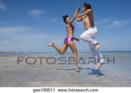 Side profile of a mid adult couple doing high-five on the beach View Large Photo Image Stock Image - Side profile of a mid adult couple doing high-five on the beach. Fotosearch