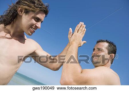 Stock Photo - Two mid adult men giving high-five to each other. Fotosearch