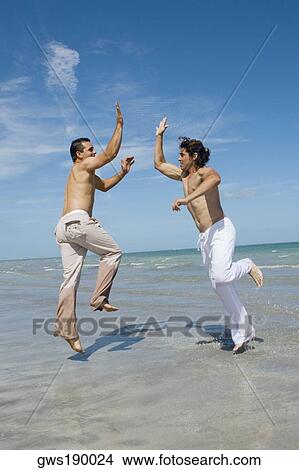 Two mid adult men jumping and giving high-five to each other on the beach View Large Photo Image Picture - Two mid adult men jumping and giving high-five to each other on the beach. Fotosearch