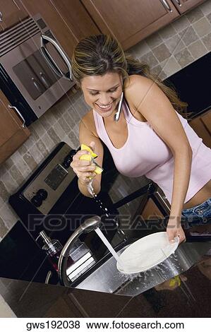 Stock Photo - Close-up of a young woman cleaning a plate while talking on a mobile phone. Fotosearch