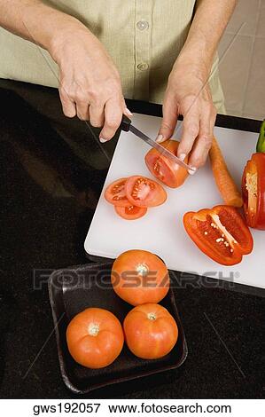 Stock Photo - Mid section view of a woman cutting vegetables on a cutting board in the kitchen. Fotosearch