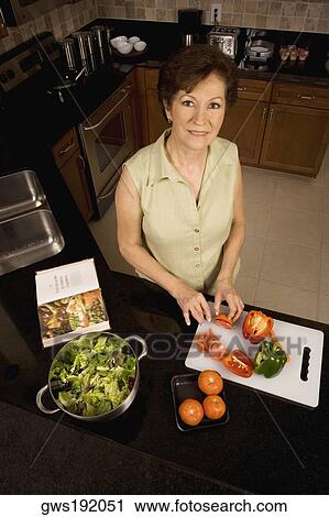 Stock Image - Portrait of a senior woman cutting vegetables on a cutting board in the kitchen. Fotosearch