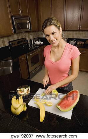 Portrait of a young woman cutting fruits on a cutting board and smiling View Large Photo Image Stock Photo - Portrait of a young woman cutting fruits on a cutting board and smiling. Fotosearch