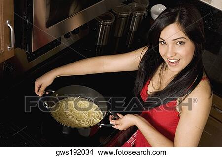 Picture - Portrait of a young woman holding a wok of noodles in the kitchen. Fotosearch