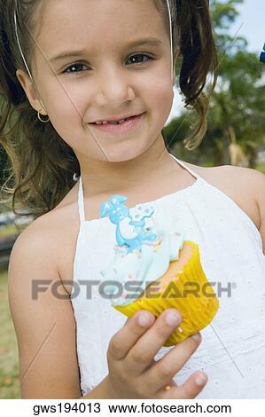 Stock Image - Portrait of a girl holding a cupcake and smiling. Fotosearch