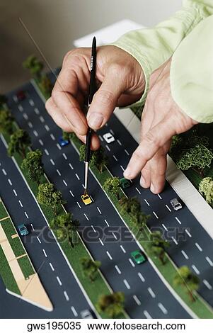 Stock Photography - Close-up of a person's hand placing a car on a model of highway. Fotosearch