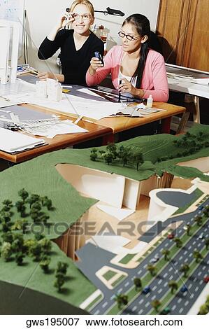 Female architect operating a mobile phone with another architect smiling beside her View Large Photo Image Stock Photo - Female architect operating a mobile phone with another architect smiling beside her. Fotosearch