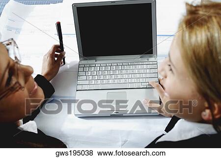 High angle view of two businesswomen working on a laptop and smiling View Large Photo Image Stock Photo - High angle view of two businesswomen working on a laptop and smiling. Fotosearch