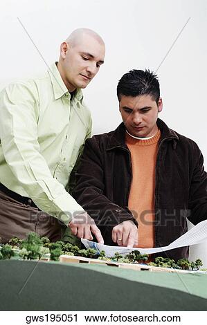 Stock Image - Two architects standing near a model and discussing a blueprint. Fotosearch