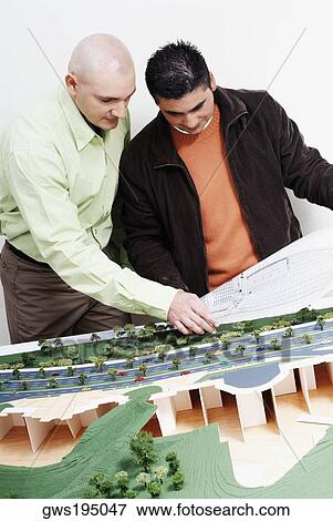 Two architects standing near a model and discussing a blueprint View Large Photo Image Stock Photo - Two architects standing near a model and discussing a blueprint. Fotosearch
