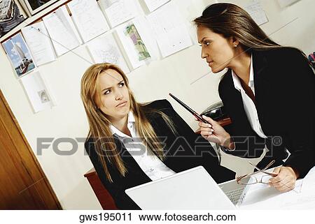 Two businesswomen talking to each other in an office View Large Photo Image Stock Image - Two businesswomen talking to each other in an office. Fotosearch