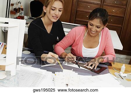 Stock Photography - Two female architects drawing a blueprint and smiling. Fotosearch