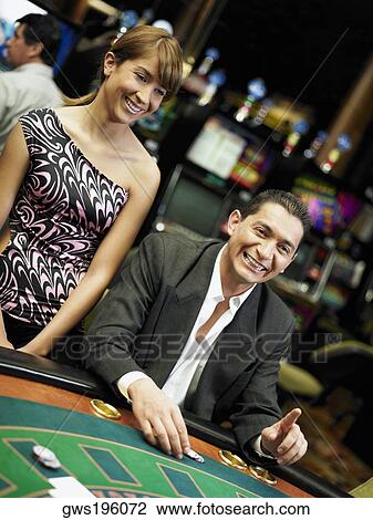 Mid adult man gambling in a casino and a young woman standing beside him View Large Photo Image Stock Image - Mid adult man gambling in a casino and a young woman standing beside him. Fotosearch