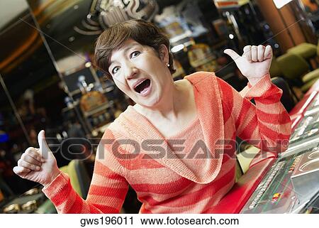 Portrait of a mature woman showing a thumbs up sign sitting in front of a slot machine View Large Photo Image Stock Image - Portrait of a mature woman showing a thumbs up sign sitting in front of a slot machine. Fotosearch