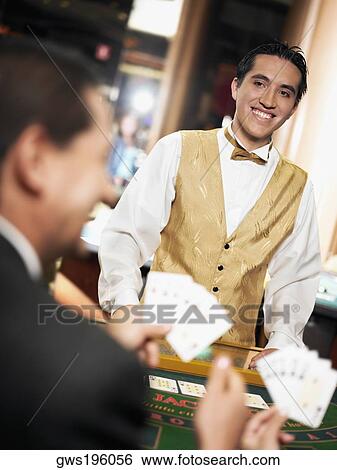 Rear view of a mature man holding playing cards with a casino worker standing in front of him View Large Photo Image Stock Photograph - Rear view of a mature man holding playing cards with a casino worker standing in front of him. Fotosearch