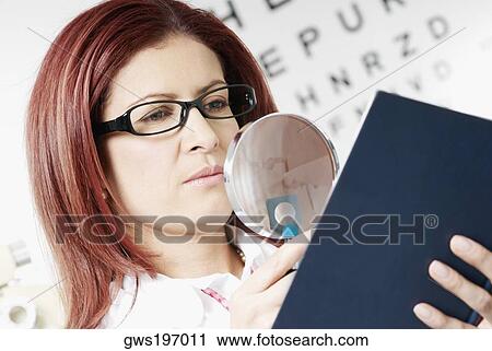 Stock Image - Close-up of a female optometrist examining a report with a magnifying glass. Fotosearch