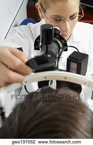 Stock Image - Close-up of a female optometrist examining eyes of a patient. Fotosearch