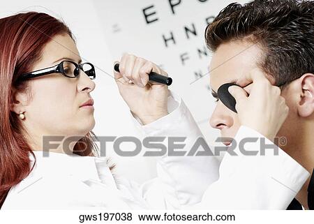 Stock Photo - Close-up of a female optometrist examining eyes of a young man. Fotosearch