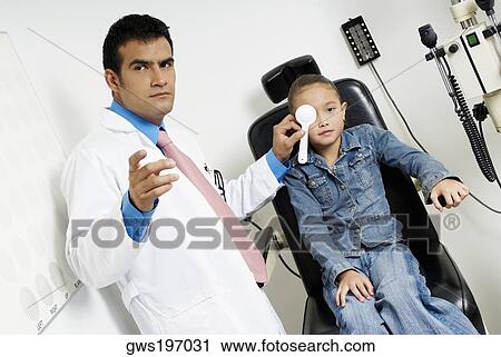 Stock Image - Male optometrist examining a girl's eye. Fotosearch