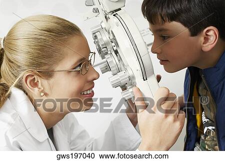 Stock Image - Side profile of a female optometrist examining a boy's eye. Fotosearch