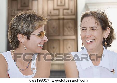 Stock Photo - Close-up of a mid adult woman sitting with a mature woman and laughing. Fotosearch