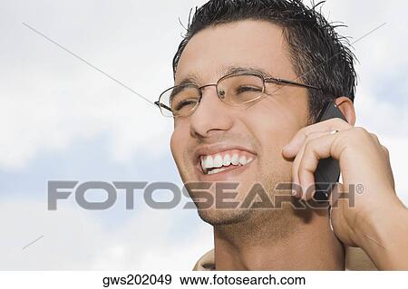 Close-up of a young man talking on a mobile phone and smiling View Large Photo Image Stock Photo - Close-up of a young man talking on a mobile phone and smiling. Fotosearch