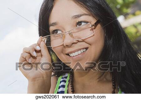 Close-up of a young woman adjusting her eyeglasses and smiling View Large Photo Image Stock Image - Close-up of a young woman adjusting her eyeglasses and smiling. Fotosearch