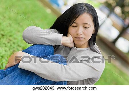 Close-up of a young woman sitting with her eyes closed in a park View Large Photo Image Stock Image - Close-up of a young woman sitting with her eyes closed in a park. Fotosearch