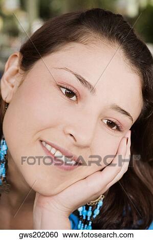 Stock Image - Close-up of a young woman smiling with her hand on her chin. Fotosearch