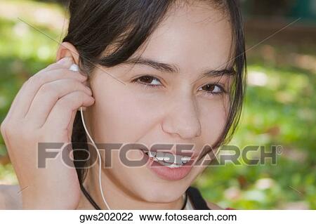 Portrait of a young woman holding an earbud and smiling View Large Photo Image Stock Image - Portrait of a young woman holding an earbud and smiling. Fotosearch