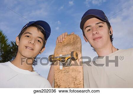 Portrait of two young men standing with a skateboard View Large Photo Image Stock Photograph - Portrait of two young men standing with a skateboard. Fotosearch